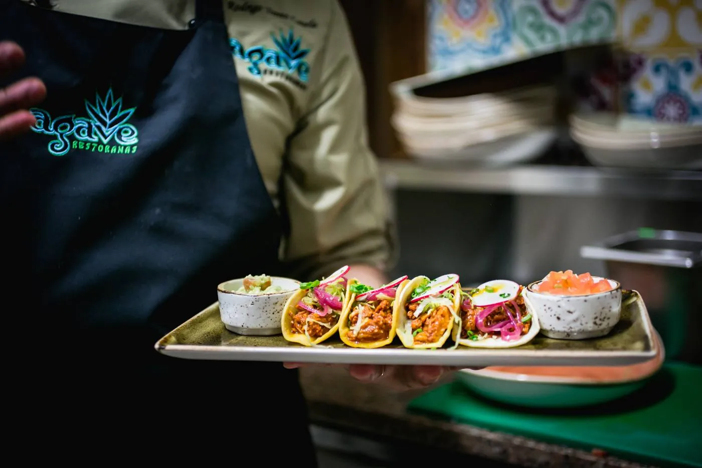 Chef Rodrigo in an Agave apron carrying a tray of tacos