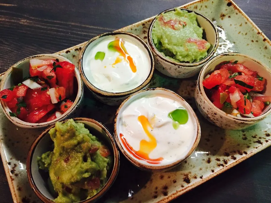 Šeši padažų indeliai ant lėkštės: pico de gallo, guacamole ir grietinės padažas su čili
